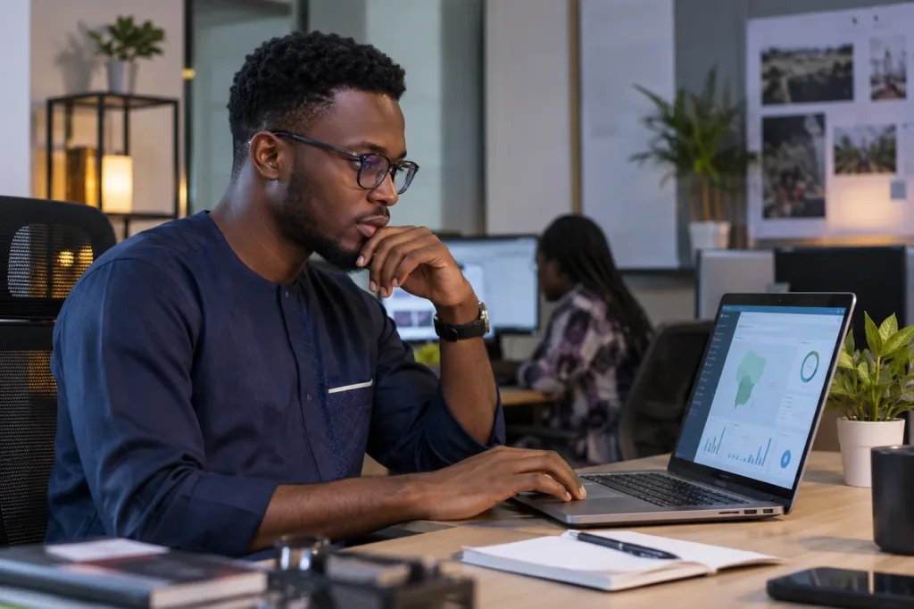 A young Nigerian technologist reviewing a ministry dashboard on a laptop in a shared workspace